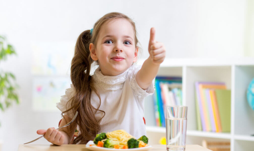 παιδί κορίτσι τρώει υγιεινά τρόφιμα που δείχνουν τον αντίχειρα επάνω στο νηπιαγωγείο