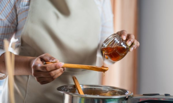Female hands holding a bowl of bee honey and a wooden spoon.